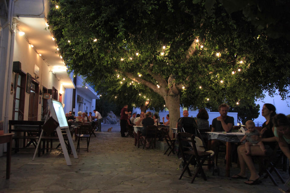 In this photo dated Monday, Aug. 6, 2018, people eat in a tavern in the Aegean island of Tilos, Greece. When the blades of the 800 kilowatt wind turbine start turning, Tilos will become the first island in the Mediterranean to run exclusively on wind and solar power. (AP Photo/ Iliana Mier)