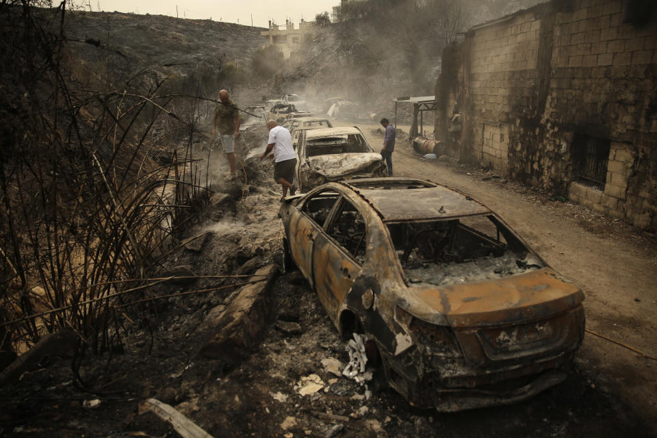 People inspect the remains of cars and shops that were burned in a wildfire overnight, in the town of Damour just over 15km (9 miles) south of Beirut, Lebanon, Tuesday, Oct. 15, 2019. Strong fires spread in different parts of Lebanon forcing some residents to flee their homes in the middle of the night as the flames reached residential areas in villages south of Beirut. (AP Photo/Hassan Ammar)