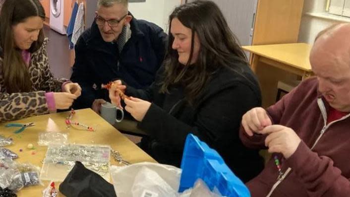 Adult learners smiling and concentrating at a table threading beads to make necklaces and breacelets