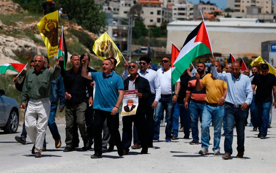 Palestinian protesters wave their national flag and portraits of prominent prisoner and popular leader Marwan Barghouti, during a demonstration in solidarity with Palestinian prisoners on hunger strike in Israeli jails - Credit: AFP PHOTO / ABBAS MOMANI