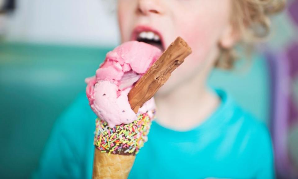 A child licking a strawberry ice-cream cone with a chocolate flake.