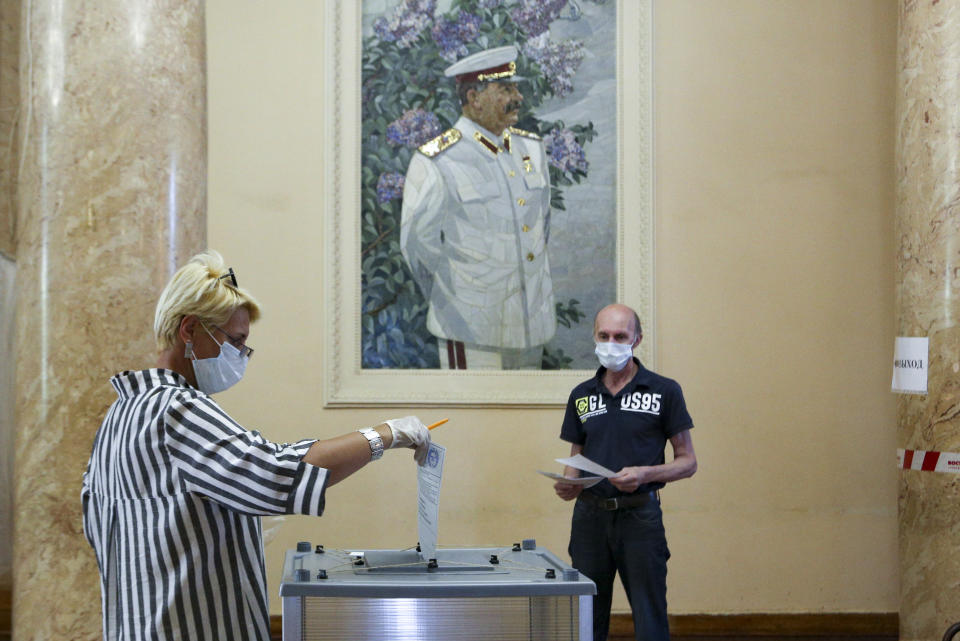 A woman, wearing a face mask and gloves to protect against coronavirus and observing social distancing guidelines, casts her ballot at a polling station with a portrait of former Soviet leader Josef Stalin on the wall in Volgograd, former Stalingrad, Russia, Wednesday, July 1, 2020. The vote on the constitutional amendments that would reset the clock on Russian President Vladimir Putin's tenure and enable him to serve two more six-year terms is set to wrap up Wednesday. (AP Photo/Dmitry Rogulin)