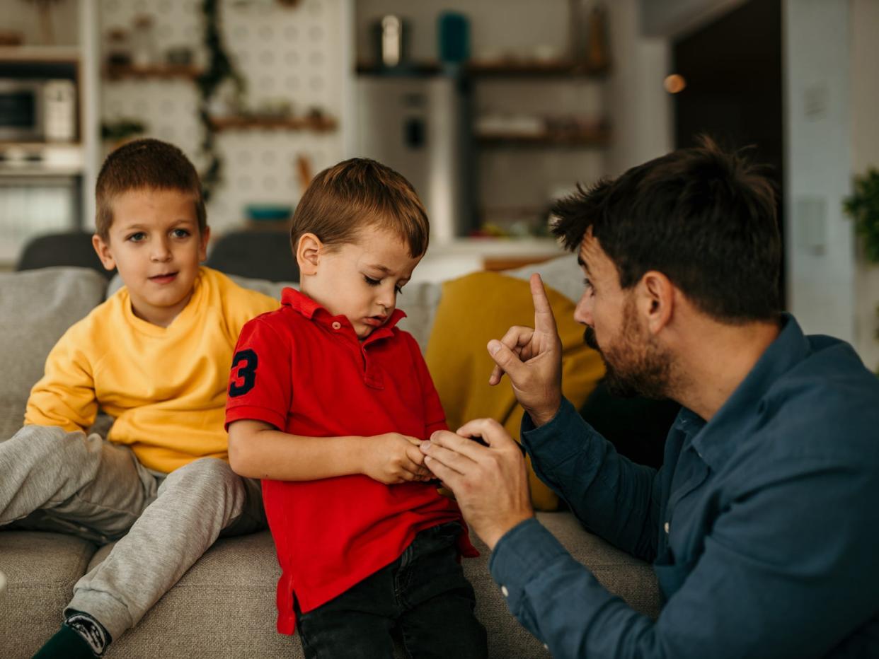 A father scolding his young son while the other son is watching