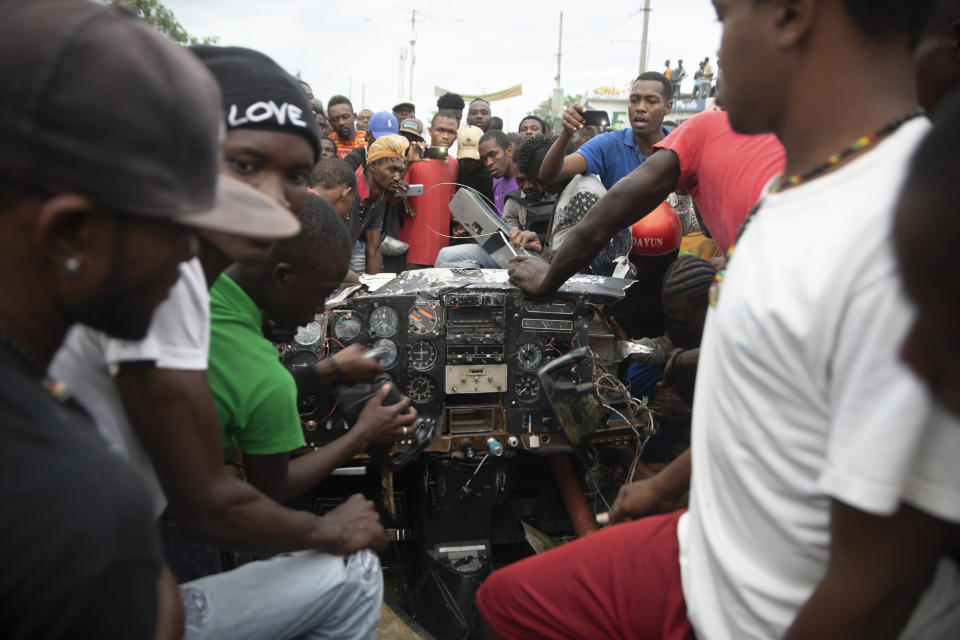 Onlookers play with the instrument panel of a small plane that crashed in the community of Carrefour, Port-au-Prince, Haiti, Wednesday, April 20, 2022. Police report that the plane was headed to the southern coastal city of Jacmel when it tried to land in Carrefour and that at least 5 people died in the accident. (AP Photo/Odelyn Joseph)