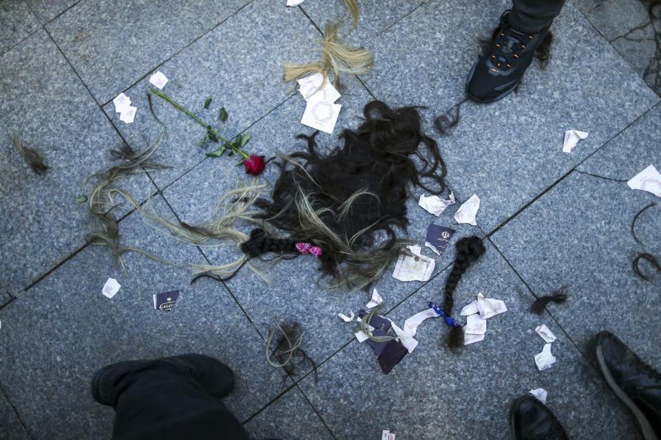 Piles of dark hair and wisps of lighter colors lie on the ground near a long-stemmed red rose