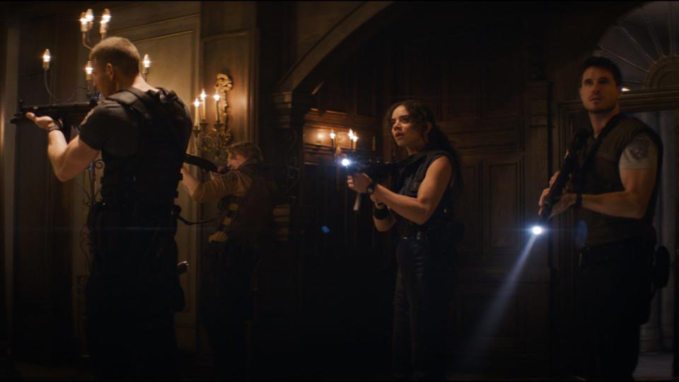 Three people in a dark room hold guns and flashlights