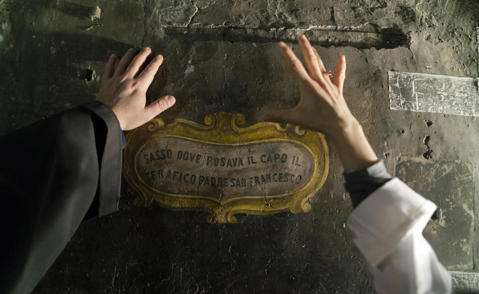 Restorer Alessia Scazzuso, right, discusses with the head of the Franciscan convent of St. Francesco a Ripa, Friar Stefano Tamburo, left, the conservation works required in the cell that St. Francis of Assisi is believed to have used when visiting the convent in Rome, during an inspection, Friday, Feb. 28, 2014. The inscription referring to a stone not shown in the picture reads in Italian: "Stone where the Serafic Father St. Francis would rest his head". The friars who run the St. Francis a Ripa church in Rome's Trastevere neighborhood are launching a Kickstarter online fundraising campaign Tuesday, March 11, 2014, to try to raise the $125,000 to restore the tiny cell upstairs from the sacristy where St. Francis stayed, The Associated Press has learned. Rather than ask for funding from the Italian government, which owns the church and is responsible for its upkeep, the friars decided on this more democratic crowdfunding initiative thinking it more in keeping with the Franciscan tradition of seeking alms for just what they need, spreading the faith as they beg, and making sure the poor are the priority. (AP Photo/Domenico Stinellis)