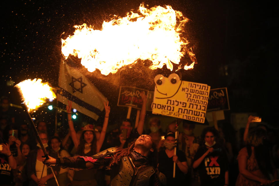 A performer dance with fire during a protest in front of Israel's Prime Minister's residence in Jerusalem, Thursday, July 16, 2020. Hundreds of protesters gathered outside Netanyahu's official residence in Jerusalem to protest against corruption and vent their anger at the economic downtown. "You are out of touch, we are fed up," one poster read. "If there's no democracy, people will get 750 shekels (about $200)," another one said, mocking the prime minister's relief package. (AP Photo/Ariel Schalit) (AP Photo/Ariel Schalit)