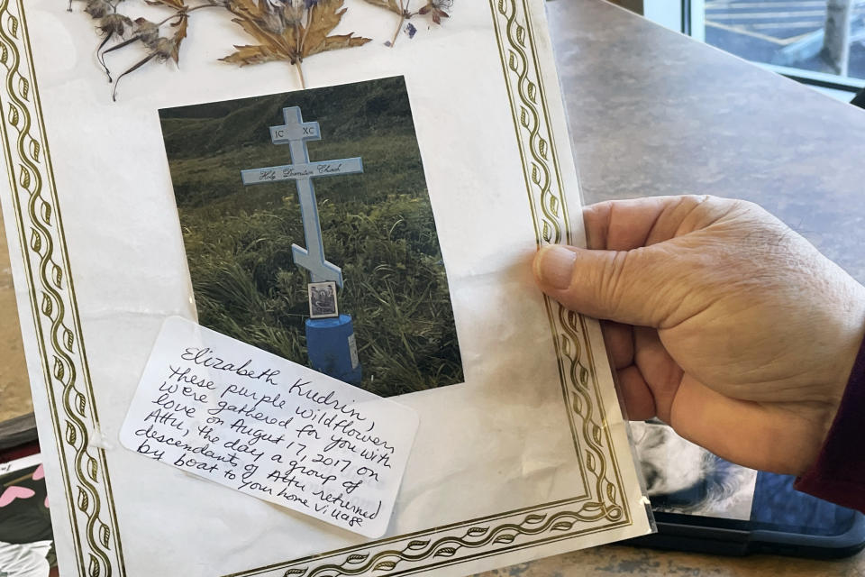 George Kudrin holds a photo of his wife's grave, Dec. 1, 2023, in Anchorage, Alaska, with flowers gathered on Attu Island pressed inside the laminate cover. His wife was the second to last living descendant of Attu, Alaska, whose entire population was captured by the Japanese during World War II and sent to Japan until being liberated after the war. She died in February 2023, and her brother Gregory Golodoff, the last living Attu resident, died nine months after she did. (AP Photo/Mark Thiessen)