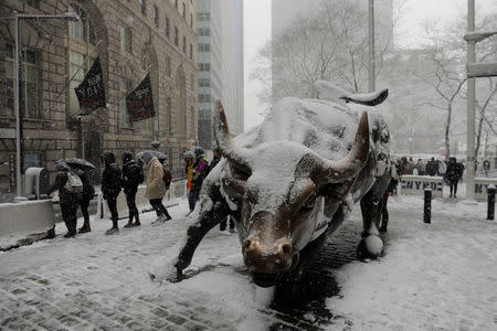 Pedestrians walk past a snow covered bull sculpture during a late season nor'easter in New York, U.S., March 21, 2018. REUTERS/Lucas Jackson