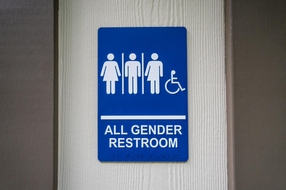 Sign on a wall reads "All Gender Restroom" with symbols for male, female, non-binary, and wheelchair accessible