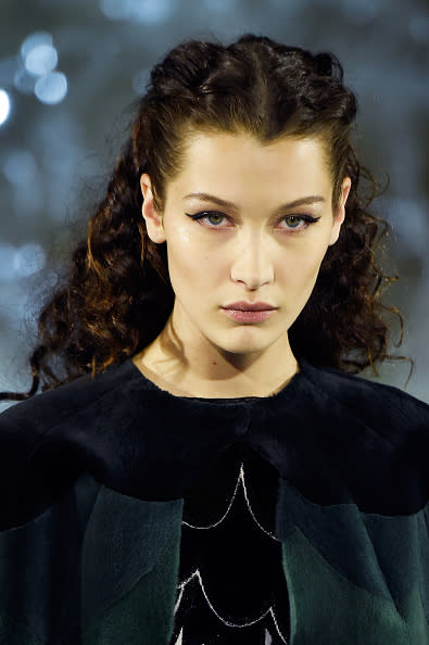 Semi-recogido para niñas con el cabello ondulado. El look de Bella Hadid consiste en hacer una raya al medio, separar las partes delanteras de la melena y llevar cada una hacia atrás. Puedes terminarlas así o hacer dos trencitas y sujetarlas con coloridos elásticos para el cabello. - Foto: Victor Boyko/Getty Images