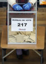 A volunteer using gloves waits for people in a polling station during local elections in Lyon, central France, Sunday, March 15, 2020. France is holding nationwide elections Sunday to choose all of its mayors and other local leaders despite a crackdown on public gatherings because of the new virus. For most people, the new coronavirus causes only mild or moderate symptoms. For some it can cause more severe illness. (AP Photo/Laurent Cipriani)