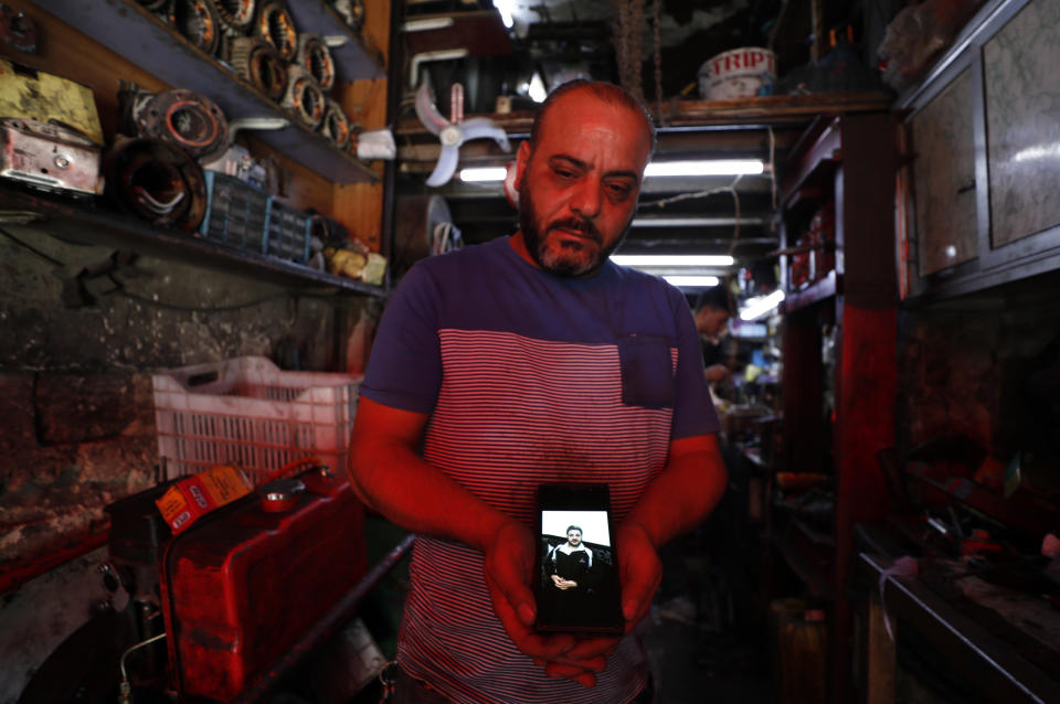 Mohammed Khier Qalaji, the brother of Firas Qalaji a Syrian man who died with his wife and his six children during the floods in the Libyan city of Derna, shows his brother picture through his mobile phone at his mechanic shop in Damascus, Syria, Saturday, Sept. 16, 2023. Firas Qalaji, 45, a car mechanic, had been living in Libya since 2000 and his wife Rana Khateeb and their six children were to be buried in Libya, the family said in a statement. (AP Photo/Omar Sanadiki)