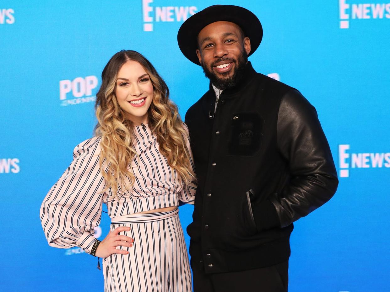 Allison Holker and Stephen "tWitch" Boss stand in front of a blue "E! News" background,