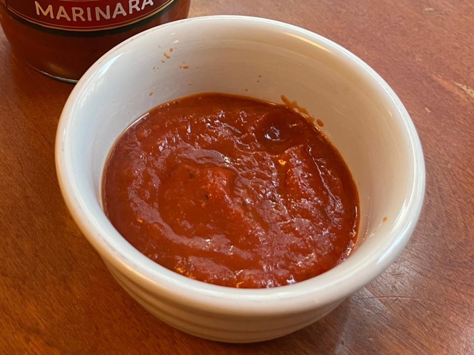 White bowl of Newman's Own marinara sauce next to jar of sauce on a wood table