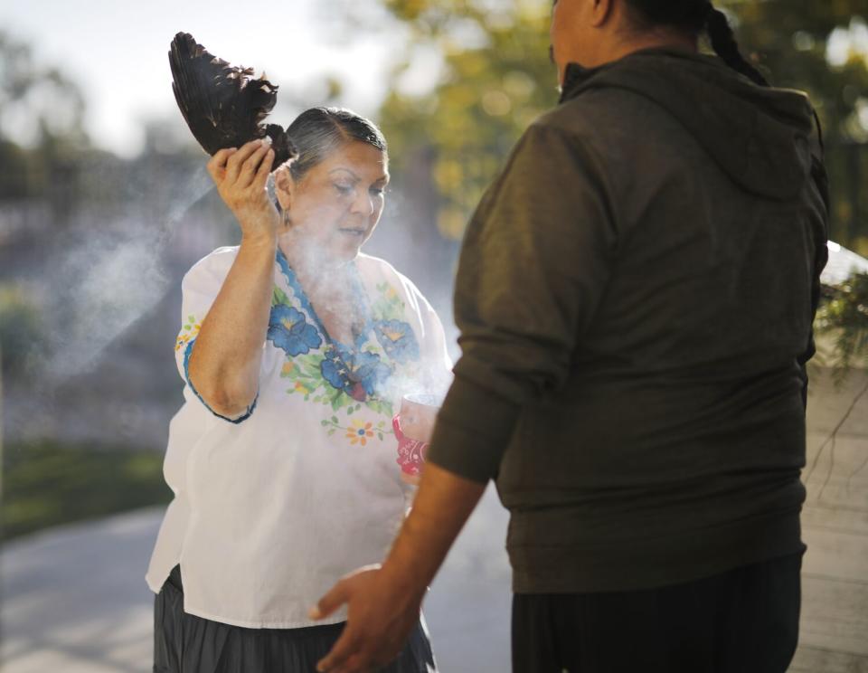 Smoke rises from a vessel held by a curandera, as a client stands with his arms open.