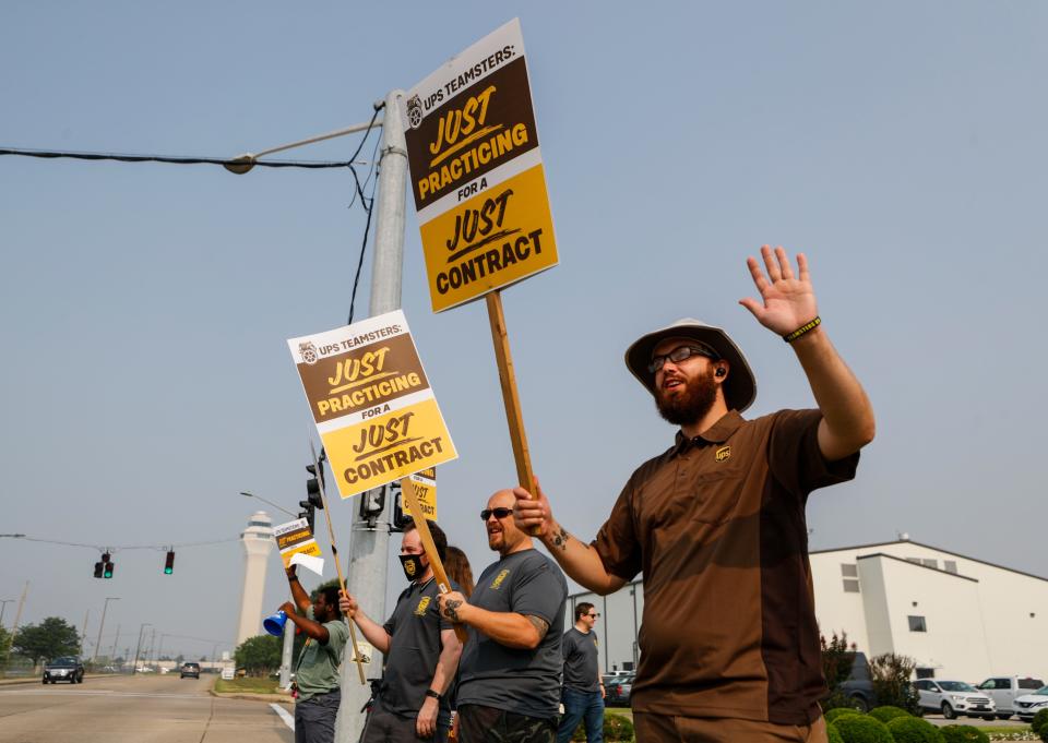 UPS worker Chris Wallace, right, waves at drivers as he and members of Teamsters Local 89 began a practice strike outside Worldport, the largest sorting and logistics facility in America on June 28 in Louisville, Ky. The International Brotherhood of Teamsters says UPS presented "an appalling economic counterproposal" during national negotiations for a new labor contract.