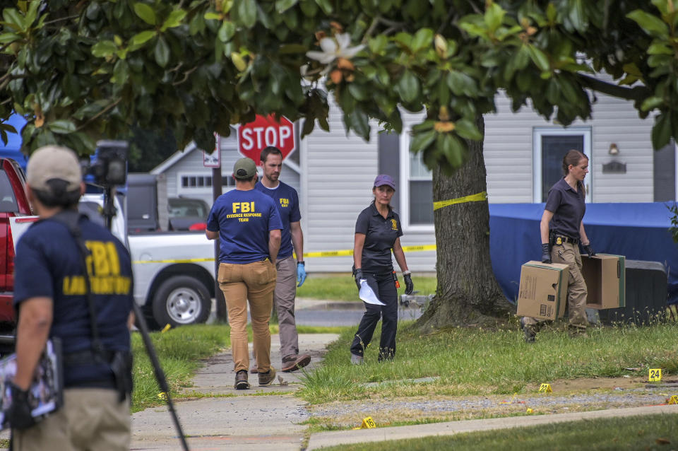 Crime scene investigators work among some of the two dozen crime scene markers scattered under a tree as law enforcement agencies gather evidence at a mass shooting that killed three people and injured three others on Monday, June 12, 2023, in Annapolis, Md. (Karl Merton Ferron/The Baltimore Sun via AP)