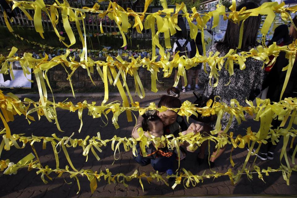 South Korean woman Lim Jung-hwa, 41, ties yellow ribbons with messages as signs of hope for safe return of missing students aboard the sunken ferry boat Sewol in the water off the southern coast, near Danwon High School in Ansan, south of Seoul, South Korea, Friday, April 25, 2014. Frustrated relatives of the scores of people still missing from the sinking of the ferry staged a marathon confrontation with the fisheries minister and the coast guard chief, surrounding the senior officials in a standoff that lasted overnight and into Friday morning as they vented their rage at the pace of search efforts. (AP Photo/Lee Jin-man)