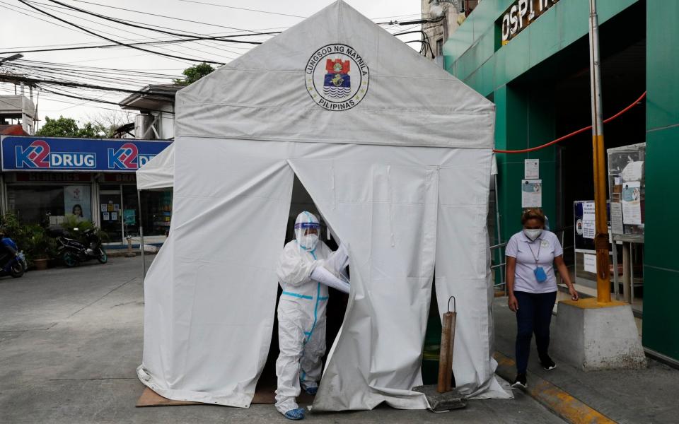 A health worker wearing a protective suit goes out of a tent with Covid-19 patients outside a hospital in Manila, Philippines - Aaron Favila/AP