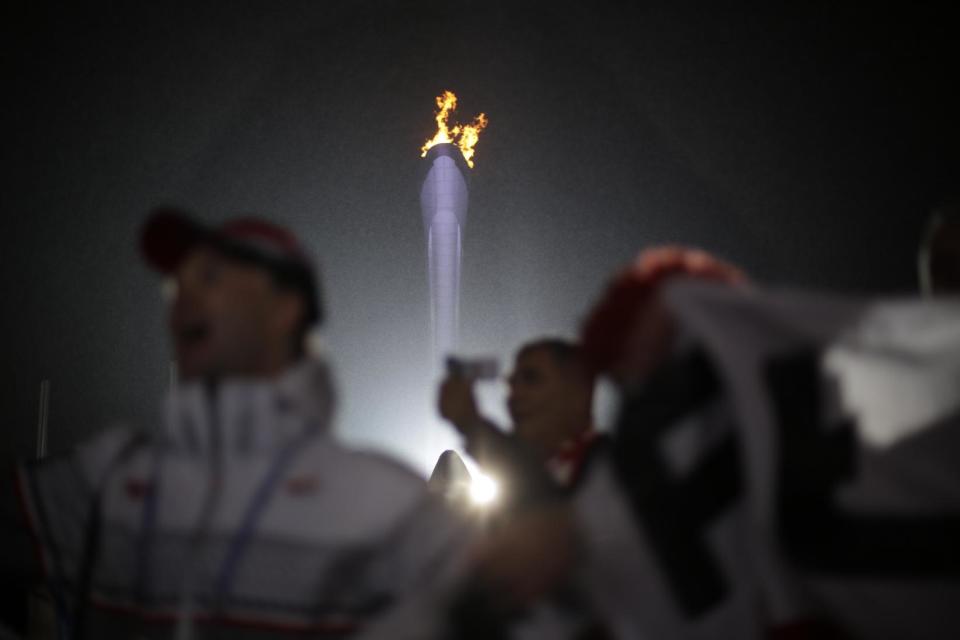 Fans cheer near the Olympic flame while watching the medals ceremonies at the 2014 Winter Olympics, Sunday, Feb. 16, 2014, in Sochi, Russia. (AP Photo/David Goldman)