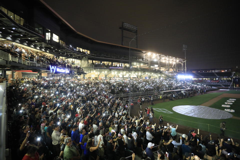 People hold up their cellphones as the names of the victims of the Aug. 3 mass shooting are read during a memorial service, Wednesday, Aug. 14, 2019, at Southwest University Park, in El Paso, Texas. (AP Photo/Jorge Salgado)