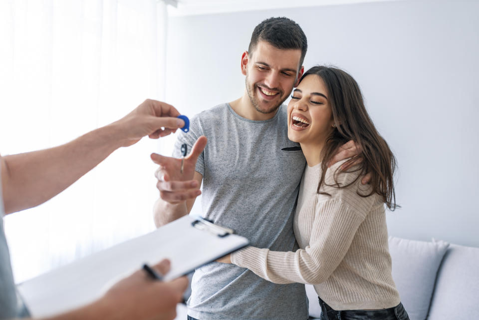 Happy couple is taking keys from their new house from broker and smiling. Hands of estate agent giving keys to the couple. The agent handed the keys a young couple