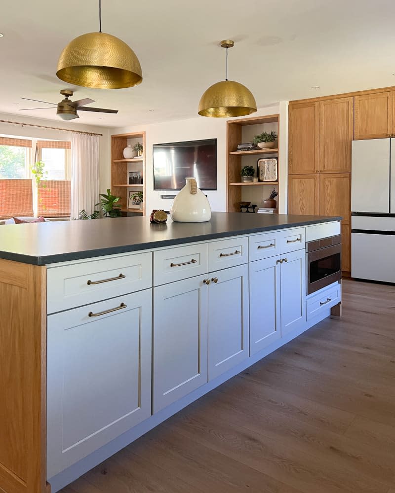 The neutral wood kitchen has a new large island with white cabinetry and black surfaces.