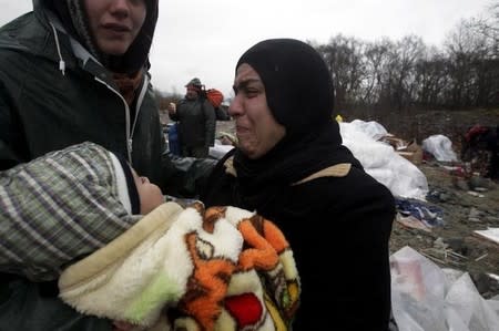 A refugee carrying her baby cries after crossing a river near the Greek-Macedonian border, west of the village of Idomeni, Greece, March 15, 2016. REUTERS/Alexandros Avramidis