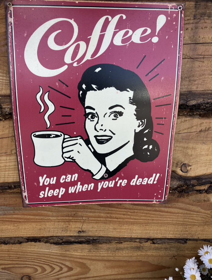 Retro sign with a smiling woman holding a coffee cup. Text reads, "Coffee! You can sleep when you're dead!"