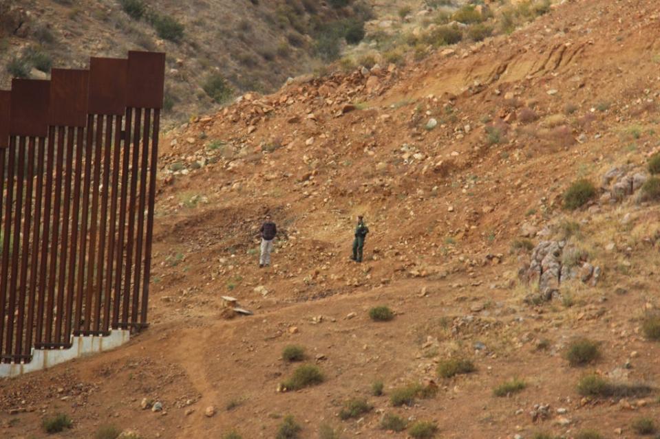 Officials speak in the gap at the US-Mexico border wall, on the outskirts of Tijuana, Mexico (The Independent)