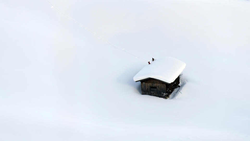 People clear a roof from snow in Lofer, Austrian province of Salzburg, Friday, Jan. 11, 2019. In Salzburg, all parks, public gardens, play areas and cemeteries were closed on Friday because of the danger of trees falling under the weight of snow.(AP Photo/Kerstin Joensson)