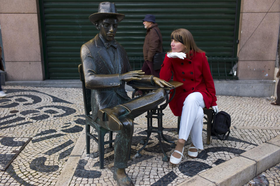 In this photo taken Jan. 1 2013, a tourist poses for a snapshot next to the statue of Portuguese poet Fernando Pessoa in Lisbon's Chiado neighborhood. The Chiado's heyday was in the late 19th-century Belle Epoque when writers and artists gathered at its cafes. Outside the Cafe A Brasileira, the statue of Fernando Pessoa, Portugal's best-known 20th-century poet who also wrote in English, is one of the city's most-photographed sights. (AP Photo/Armando Franca)