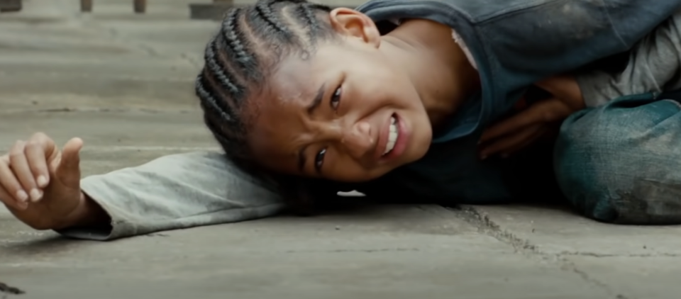 Girl lying on ground appearing distressed in a scene from a film