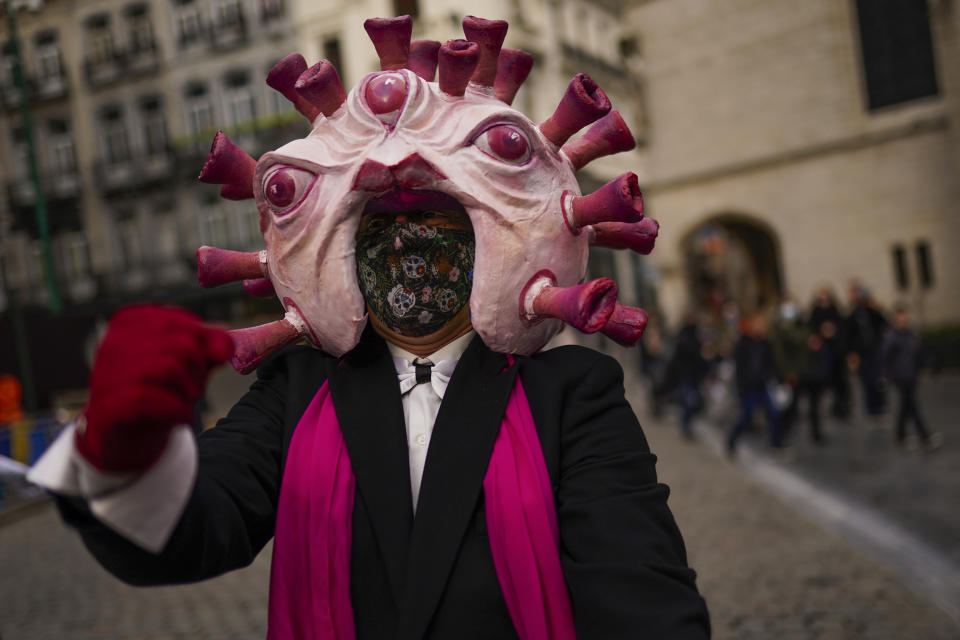 An actor, dressed up depicting a coronavirus, gestures to passers-by during a street performance promoting anti COVID-19 security measures in downtown Brussels, Thursday, Dec. 31, 2020. (AP Photo/Francisco Seco)