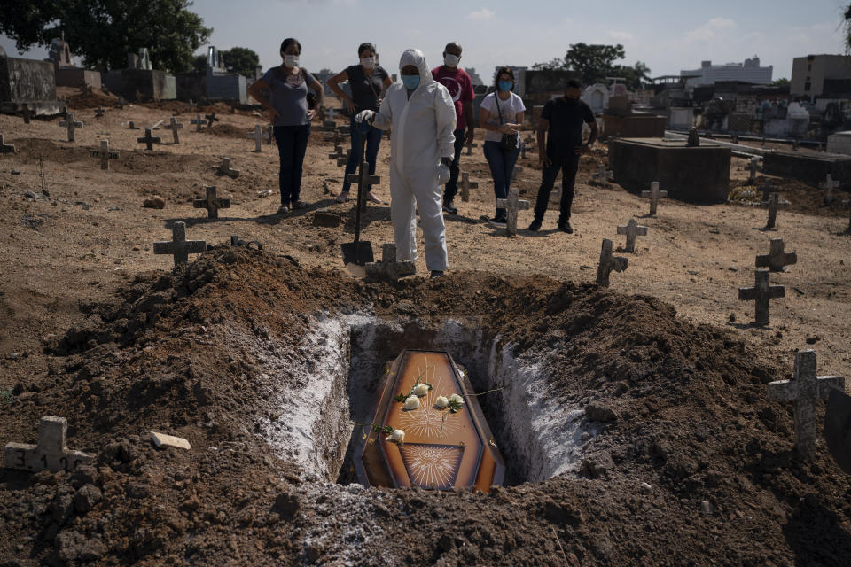 A cemetery worker stands before the coffin containing the remains of Edenir Rezende Bessa, who is suspected to have died of COVID-19, as relatives attend her burial, in Rio de Janeiro, Brazil, Wednesday, April 22, 2020. After visiting 3 primary care health units she was accepted in a hospital that treats new coronavirus cases, where she died on Tuesday. “People need to believe that this is serious, it kills", said her son Rodrigo Bessa who works at a hospital as nurse in the Espirito Santo state. (AP Photo/Leo Correa)