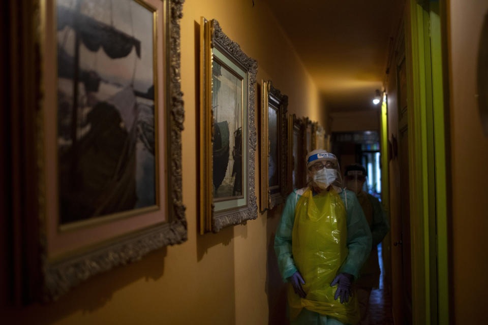 Nurse Isabel Solis, 46, wearing a converted garbage bag apron for protection, walks along a corridor lined with paintings made by Enrique Pastor, 86, during a home visit in Barcelona, Spain, April 1, 2020. Pastor's full-time caregiver tested positive for the virus, leaving his wife to care for the bedridden Pastor without knowing if either of them has COVID-19. (AP Photo/Emilio Morenatti)