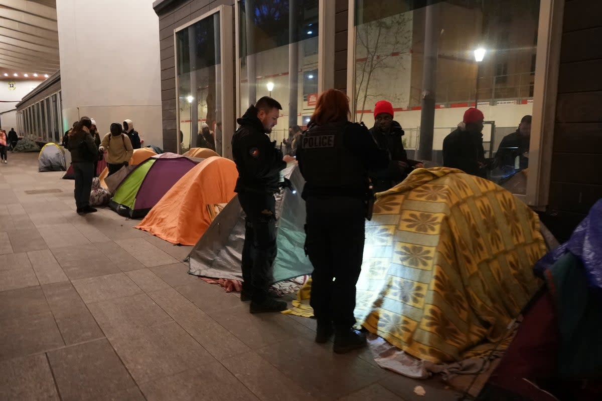 Police officers at a makeshift migrant camp in Paris, early on Tuesday, April 23 (AP)