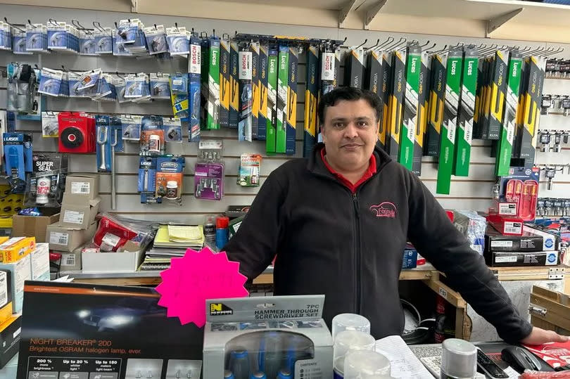 Sohaib Malik, of Formula Motor Factors, at the till in his shop in front of shelf of car parts