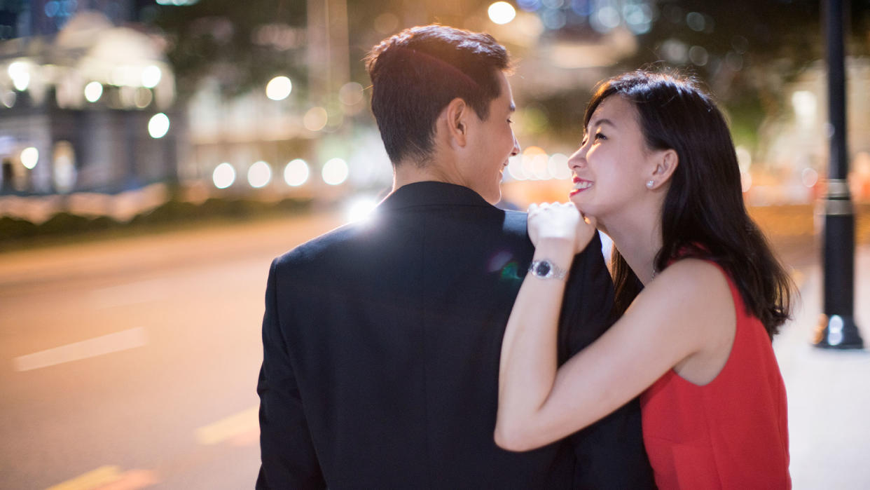 Man in suit and woman in red dress starting at each other along the streets at night. (Photo: Getty Images)