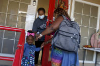 Wanda Vincent prepares to check the temperature of 2-year-old Olivia Grace Charles, who holds the hand of her mother, Guerda Philemond, outside the Mother's Heart Learning Center in Arlington, Texas, on Monday, Oct. 25, 2021. Philemond is worried about a proposal to add three new gas wells at a drill site that's a few hundred feet from the day care and several residences. The fracking site is operated by TEP Barnett, a subsidiary of French energy giant Total Energies. (AP Photo/Martha Irvine)