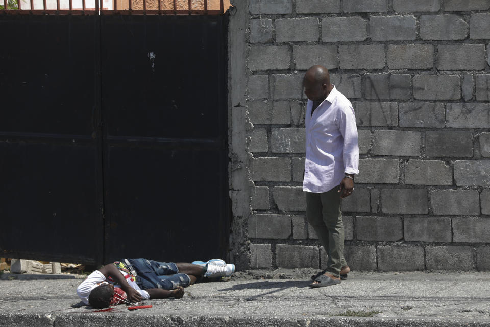 A resident looks at a body lying in the street in the Delmas area of Port-au-Prince, Haiti, Wednesday, March 20, 2024. The red item next to the body is a cell phone. (AP Photo/Odelyn Joseph)