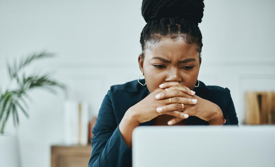 A person clasping hands and looking at a computer screen with a concerned expression. 