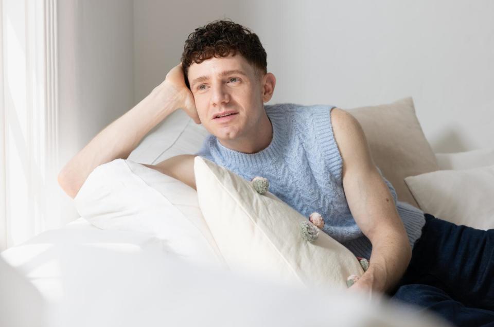 Actor Chris Perfetti, dressed in a baby blue sweater vest, lounges on a couch in his Los Angeles home.