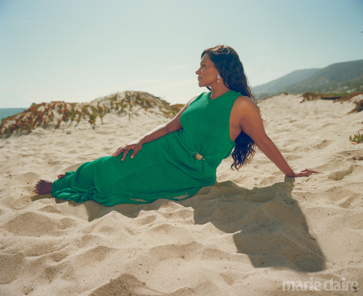 Mindy Kaling in a green dress lounging in the sand. (Photo: Kanya Iwana for Marie Claire)