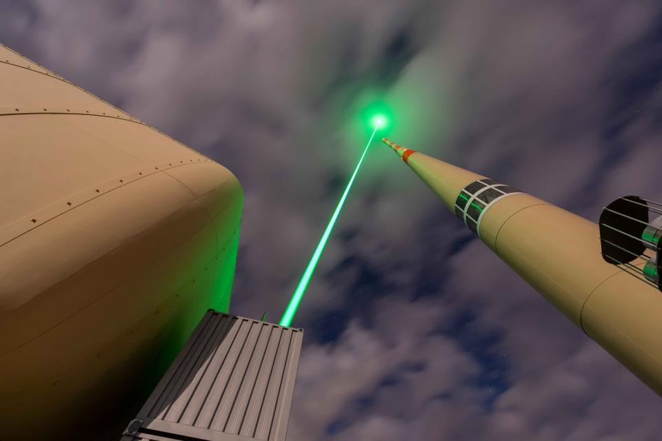 A laser is seen shooting towards the sky near a tall telecommunications tower. 