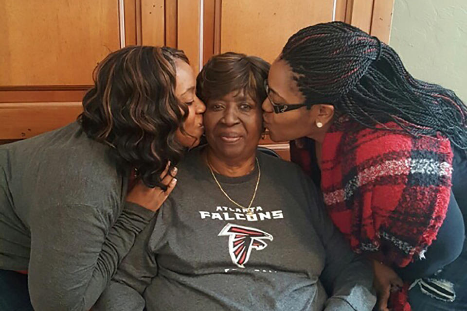 In this Feb. 1, 2017, photo provided by the Burrough Family, Bessie Burden, center, gets kisses from her daughters Theresa Burrough, left and Lashieka Mitchell in Colquitt, Ga. Burden died Oct. 22, 2020, after becoming infected with the coronavirus during an outbreak at the nursing home. Burden’s daughters blame the home for their mother’s death, saying administrators kept the family in the dark about Burden being exposed to the virus and quarantined as a presumptive case. But the state has essentially blocked them from going to court. (William Burrough via AP)