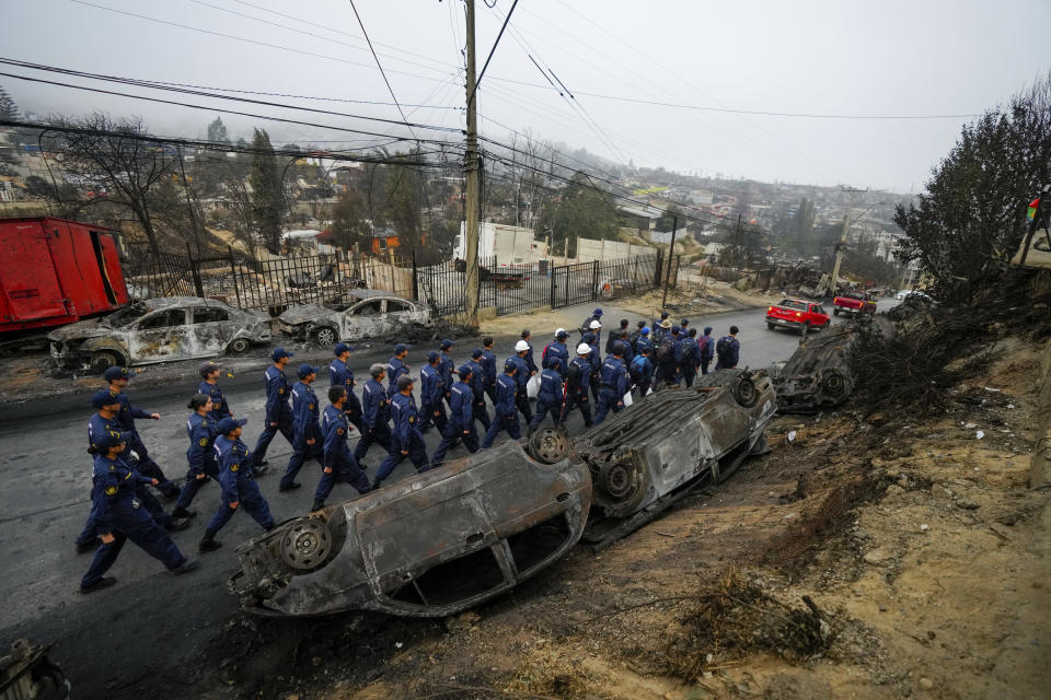 Chilean Navy personnel walk past overturned, charred cars as they deploy to help aid the Villa Independencia neighborhood affected by forest fires in Vina del Mar, Chile, Tuesday, Feb. 6, 2024. (AP Photo/Esteban Felix)
