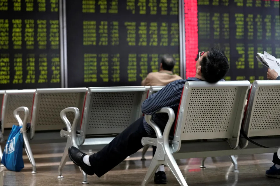 An investor takes a nap in front of a board showing stock information at a brokerage office in Beijing, China October 8, 2018. REUTERS/Jason Lee